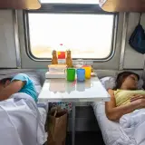 Para dowiedzieć się, ile kosztuje miejsce w wagonie sypialnym, wystarczy spojrzeć na ten widok: para śpi w przedziale, a na stole stoją napoje i kubki.