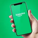 Dłoń trzyma smartfon z zielonym ekranem i logo Żappka. Sprawdzam, czy w Żabce są bilety autobusowe.