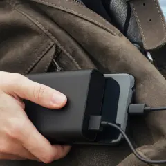 Ręka trzyma powerbank ładujący telefon. Podróżując, warto wiedzieć, czy w pociągu można ładować telefon.