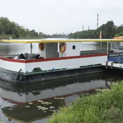 Statek do Serocka z polską flagą czeka na pasażerów. W tle widoczne są kominy elektrowni i drzewa.
