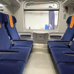 Wnętrze wagonu TLK z niebieskimi siedzeniami i pomarańczowymi zagłówkami. Obok siedzeń widać zielone lampki, co sugeruje, że czy w TLK są kontakty.