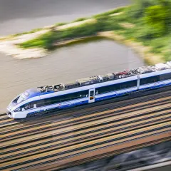 Pędzący pociąg Intercity w ruchu, z rozmytym tłem rzeki i zieleni.