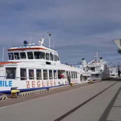Wodolot Gdynia Hel "SMILE" cumuje przy nabrzeżu. W tle inne statki i budynek z napisem "Katamrany Wodoloty Statki".