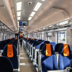 Wnętrze nowoczesnego wagonu PKP Intercity. Siedzenia w kolorze granatowym z pomarańczowymi zagłówkami. Ile wagonów ma pociąg IC? To zależy od trasy i typu składu.