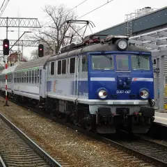 Niebieska lokomotywa EU07-067 PKP Intercity stoi na torach. Co oznacza TLK w pociągach? To oznaczenie tanich połączeń PKP Intercity.