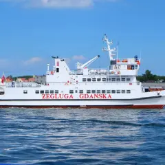 Biały tramwaj wodny "Żegluga Gdańska" płynie po morzu, w tle widać zabudowania Gdyni i Helu.