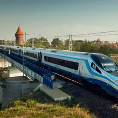 Nowoczesny pociąg Pendolino jedzie po moście nad rzeką. W tle widać zamek. Czy bilet bez wskazania miejsca jest tańszy?