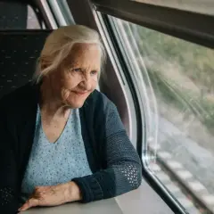 Starsza pani wpatruje się w krajobraz za oknem pociągu Pendolino, zastanawiając się, czy na pendolino są zniżki dla emerytów.