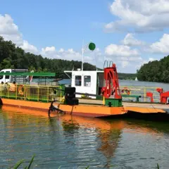 Prom na Zalewie Prężyce z białym vanem i pomarańczowym pokładem, otoczony zielonymi lasami.