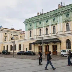 Kraków Główny. Krótki spacer z dworca na rynek, przez plac przed zabytkowym budynkiem, gdzie przechodzą ludzie.