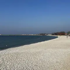 Piękna plaża, idealna na rejs z Gdańska na Hel. W oddali widać falochron i zabudowania.