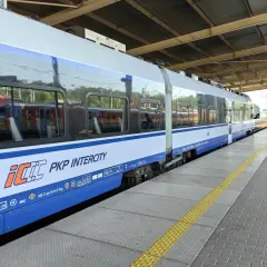 Pociąg PKP Intercity na peronie, z widocznymi odbiciami innych pociągów w oknach.