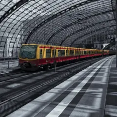 Żółto-czerwony pociąg S-Bahn Berlin stoi na nowoczesnym, zadaszonym peronie.
