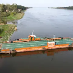 Prom "Świbno" czeka na pasażerów przy brzegu, gotowy do przeprawy przez szeroką rzekę.