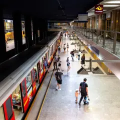 Ludzie na peronie metra, szukający drogi z dworca centralnego do metra. Widać pociąg i wejścia do sklepów.
