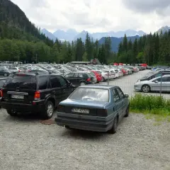 Duży parking samochodowy u podnóża gór, z widokiem na Tatry, jakby eic morskie oko patrzyło z góry.