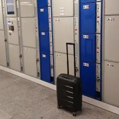 Na Dworcu Warszawa Centralna jest przechowalnia bagażu. Widać rzędy skrytek bagażowych, a obok jedna czarna walizka.