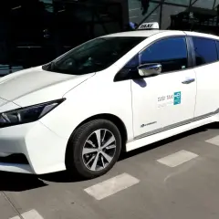 Białe taxi z lotniska Balice, elektryczne, gotowe do jazdy. Zastanawiasz się, ile kosztuje taxi z lotniska Balice do centrum Krakowa?