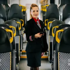 Uśmiechnięta konduktorka w mundurze stoi między rzędami siedzeń w pociągu. Czy u konduktora można płacić blikiem?