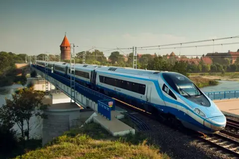 Nowoczesny pociąg Pendolino jedzie po moście nad rzeką. W tle widać zamek. Czy bilet bez wskazania miejsca jest tańszy?
