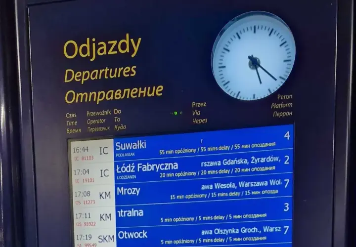 Tablica odjazdów pociągów pokazuje, gdzie sprawdzić opóźnienia pociągu. Widoczne są czasy, kierunki i informacje o opóźnieniach.