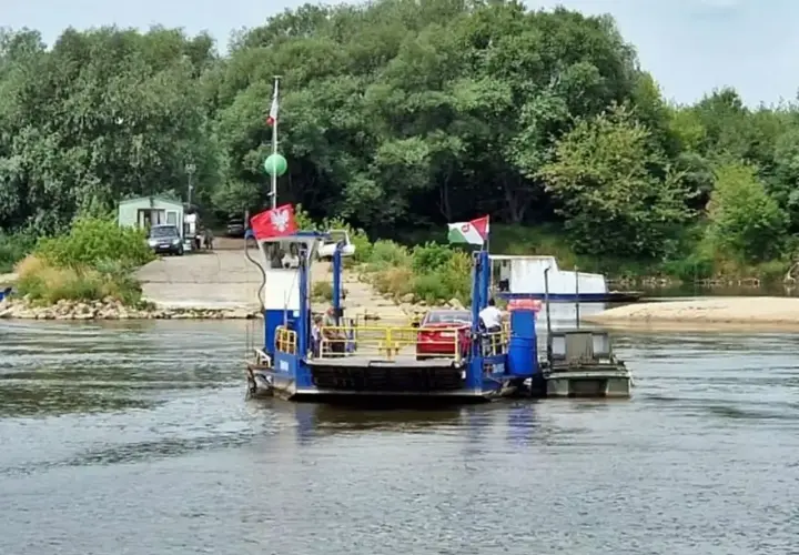 Prom gassy Karczew przeprawia się przez rzekę. Na pokładzie widać czerwony samochód i ludzi.