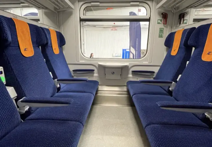 Wnętrze wagonu TLK z niebieskimi siedzeniami i pomarańczowymi zagłówkami. Obok siedzeń widać zielone lampki, co sugeruje, że czy w TLK są kontakty.
