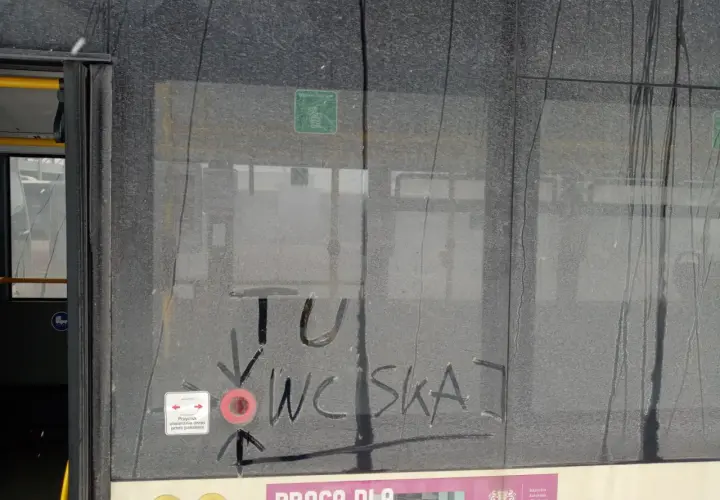 Brudne drzwi pociągu z napisem "TU WCISKAJ" i ikoną przycisku otwierania drzwi.