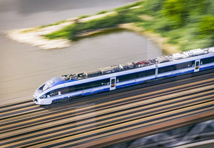 Pędzący pociąg Intercity w ruchu, z rozmytym tłem rzeki i zieleni.