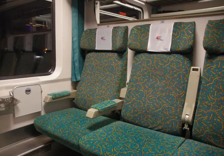 Wagon bez przedziałów PKP Intercity. Rozkład miejsc: dwa siedzenia obok siebie, tapicerka w turkusowo-pomarańczowe wzory.