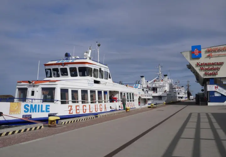 Wodolot Gdynia Hel "SMILE" cumuje przy nabrzeżu. W tle inne statki i budynek z napisem "Katamrany Wodoloty Statki".