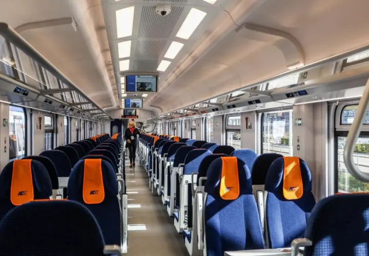 Wnętrze nowoczesnego wagonu PKP Intercity. Siedzenia w kolorze granatowym z pomarańczowymi zagłówkami. Ile wagonów ma pociąg IC? To zależy od trasy i typu składu.