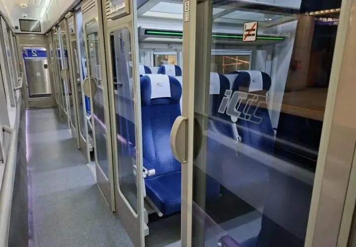 Wnętrze pociągu Intercity. Widać rząd niebieskich siedzeń i drzwi. Na szybie znak zakazu palenia, więc nie ma palarni.