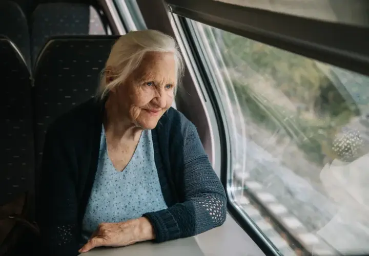 Starsza pani wpatruje się w krajobraz za oknem pociągu Pendolino, zastanawiając się, czy na pendolino są zniżki dla emerytów.
