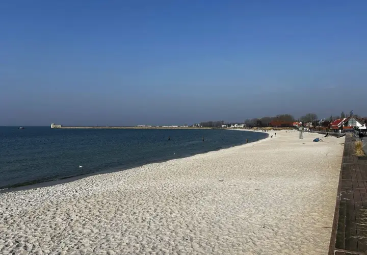 Piękna plaża, idealna na rejs z Gdańska na Hel. W oddali widać falochron i zabudowania.