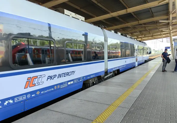 Pociąg PKP Intercity na peronie, z widocznymi odbiciami innych pociągów w oknach.