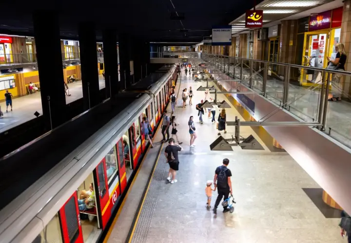Ludzie na peronie metra, szukający drogi z dworca centralnego do metra. Widać pociąg i wejścia do sklepów.