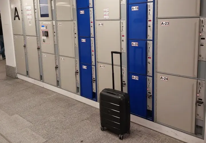 Na Dworcu Warszawa Centralna jest przechowalnia bagażu. Widać rzędy skrytek bagażowych, a obok jedna czarna walizka.