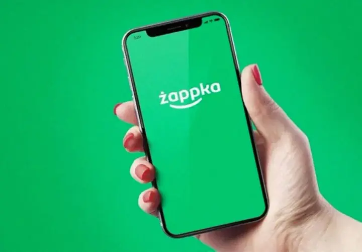 Dłoń trzyma smartfon z zielonym ekranem i logo Żappka. Sprawdzam, czy w Żabce są bilety autobusowe.
