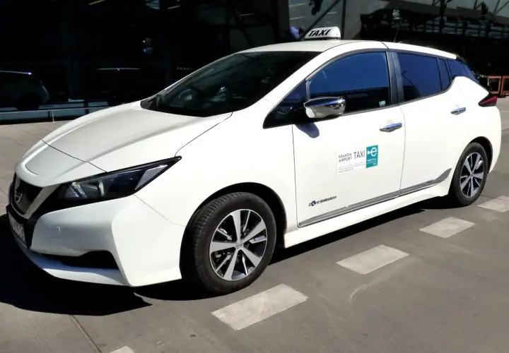 Białe taxi z lotniska Balice, elektryczne, gotowe do jazdy. Zastanawiasz się, ile kosztuje taxi z lotniska Balice do centrum Krakowa?