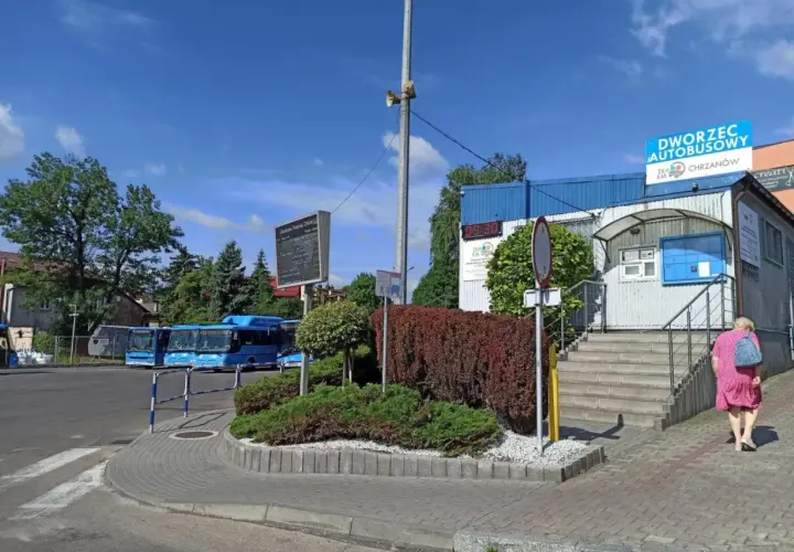 Chrzanów dworzec autobusowy. Niebieskie autobusy czekają na pasażerów, a kobieta w różowej sukience idzie w stronę budynku.
