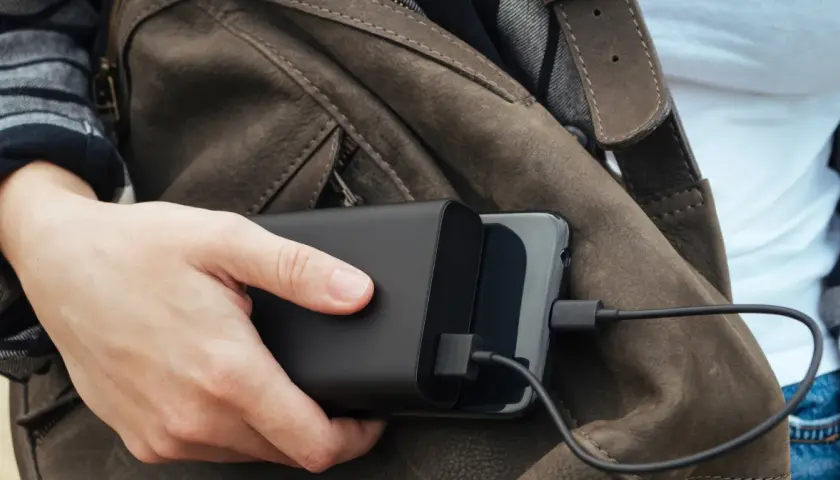 Ręka trzyma powerbank ładujący telefon. Podróżując, warto wiedzieć, czy w pociągu można ładować telefon.