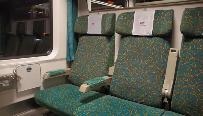 Wagon bez przedziałów PKP Intercity. Rozkład miejsc: dwa siedzenia obok siebie, tapicerka w turkusowo-pomarańczowe wzory.