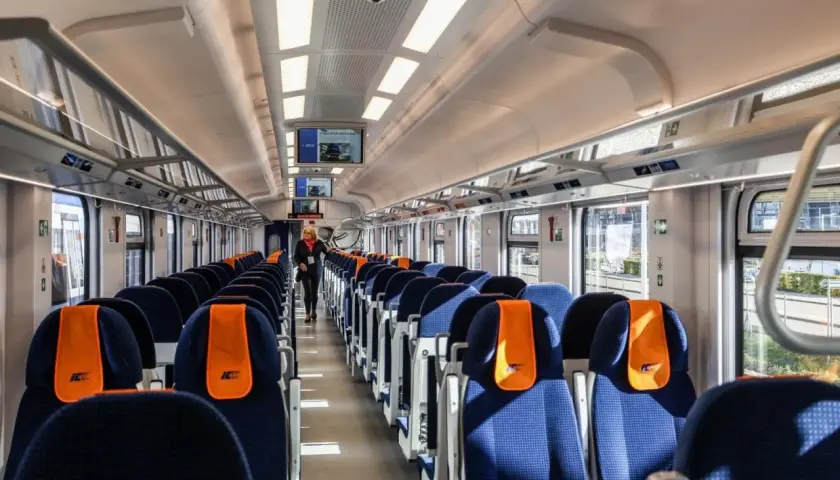 Wnętrze nowoczesnego wagonu PKP Intercity. Siedzenia w kolorze granatowym z pomarańczowymi zagłówkami. Ile wagonów ma pociąg IC? To zależy od trasy i typu składu.