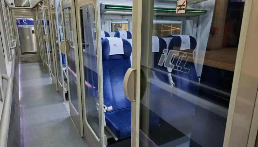 Wnętrze pociągu Intercity. Widać rząd niebieskich siedzeń i drzwi. Na szybie znak zakazu palenia, więc nie ma palarni.