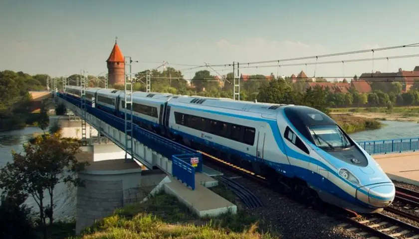 Nowoczesny pociąg Pendolino jedzie po moście nad rzeką. W tle widać zamek. Czy bilet bez wskazania miejsca jest tańszy?