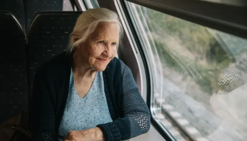 Starsza pani wpatruje się w krajobraz za oknem pociągu Pendolino, zastanawiając się, czy na pendolino są zniżki dla emerytów.