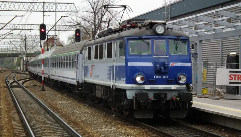 Niebieska lokomotywa PKP Intercity EU07-067 z wagonami na torach kolejowych.