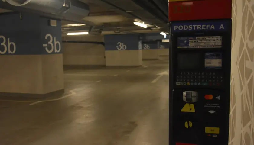 Podziemny parking na dworcu fabrycznym jest płatny. Widać parkingowy automat z klawiaturą i opcjami płatności.