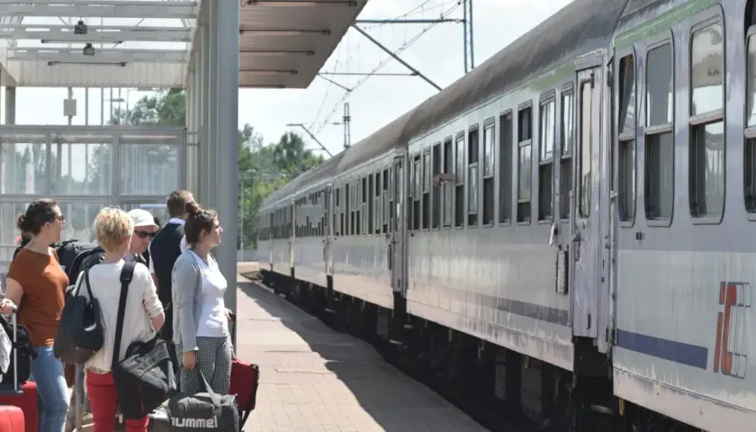 Ludzie czekają na pociąg PKP. Zastanawiają się, ile wynosi zniżka uczniowska PKP, by podróżować taniej.